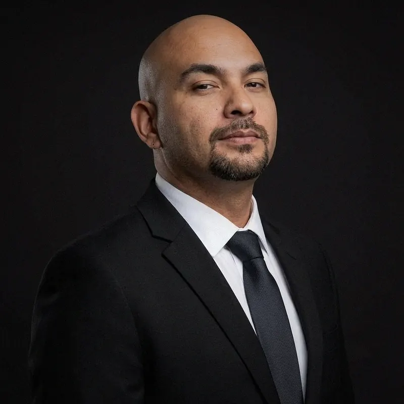 Fernando Castro in a black suit and tie against a dark background.
